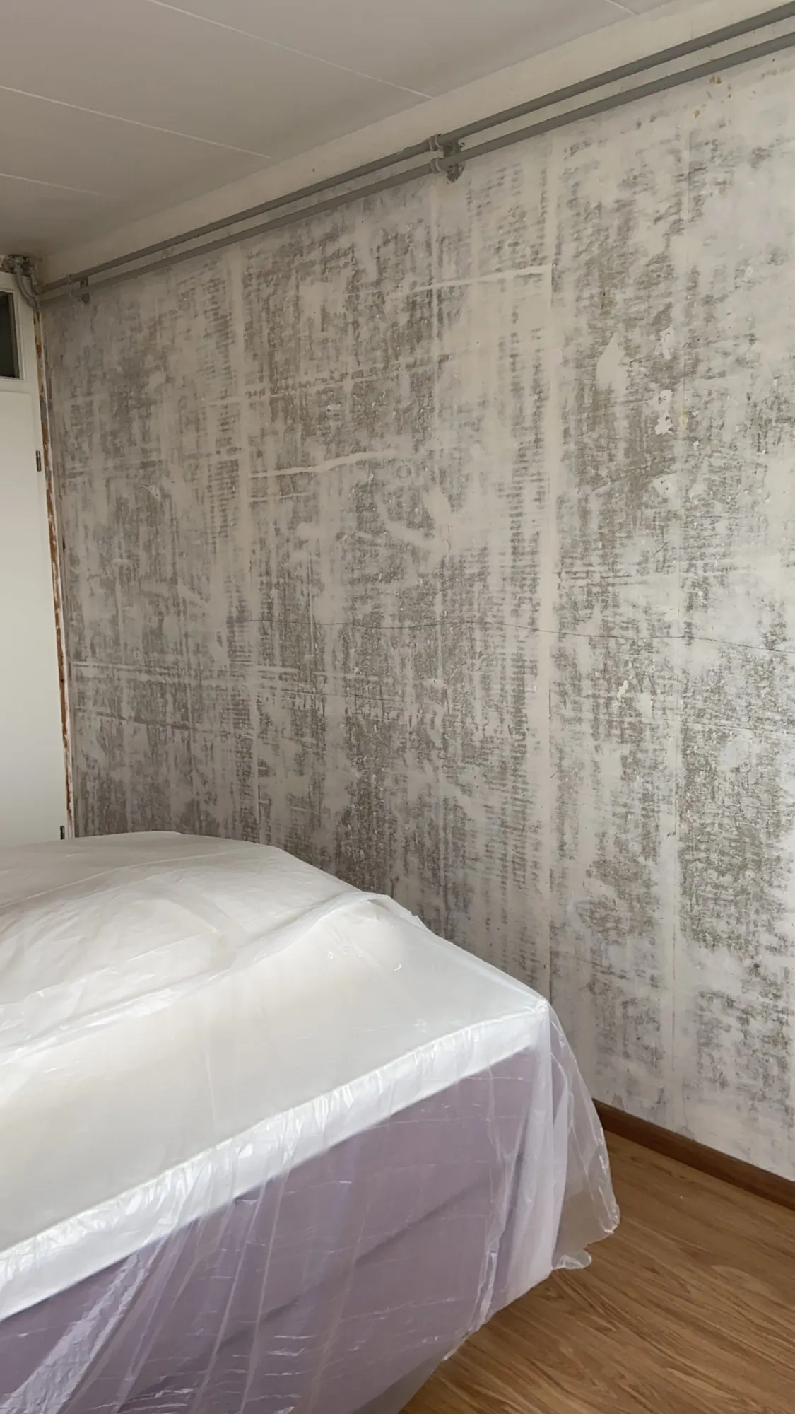 Wand met een strakke betonlook-structuur naast een bed